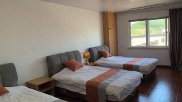 Een hotelkamer met twee bedden, een nachtkastje, een raam met gordijnen en uitzicht op groen.