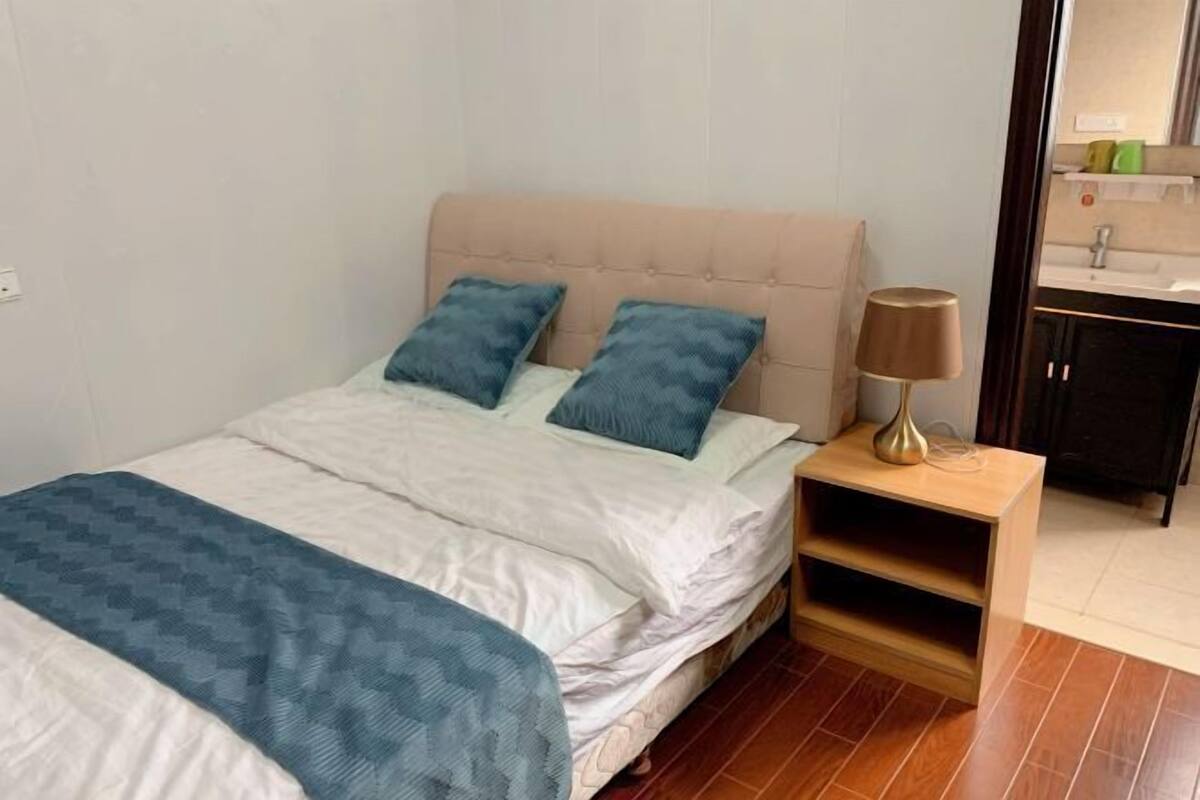 A bedroom with a bed, two pillows, a bedside table with a lamp, and a wooden nightstand.
