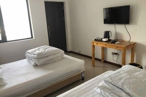 Una habitación con dos camas, un televisor, una mesa con hervidor y una puerta.