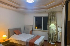 A bedroom with a bed, bedside lamp, window with curtains, and a standing lamp. - Haipai Inn (Pingyang)