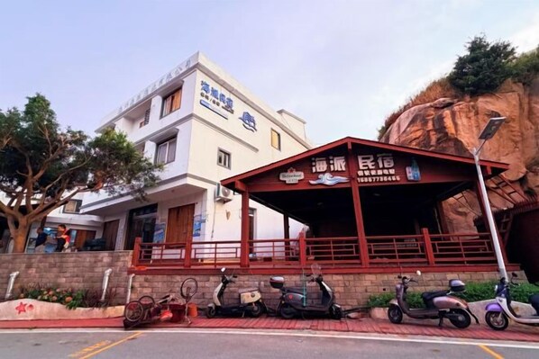 A building with a covered outdoor seating area, a signboard, and several scooters parked in front. - Haipai Inn (Pingyang)