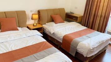 A hotel room with two beds, a nightstand with a lamp, a wooden side table, and a window with curtains.