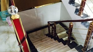 Uma escadaria de mármore com corrimão em vermelho e dourado, degraus em preto e branco, e uma esfera de vidro transparente no corrimão.