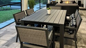 A modern outdoor dining area with a large table and wicker chairs, overlooking a pool and palm trees. - Hidden Gem with Jacuzzi, Waterfront   (North Port)