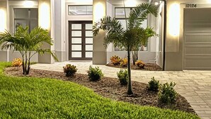 A modern house with a well-lit entrance, a garage, and a landscaped front yard with small trees and grass. - Hidden Gem with Jacuzzi, Waterfront   (North Port)
