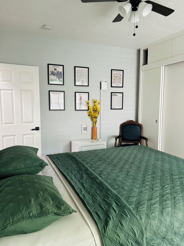 Une chambre à coucher avec un lit, des oreillers, une chaise, un bureau et des tableaux encadrés accrochés au mur.