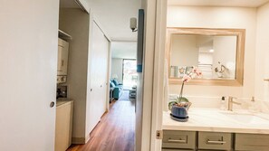 Une chambre d’hôtel avec un plancher en bois, une salle de bain dotée d’un grand miroir et d’un lavabo, et une vue sur le couloir et l’espace salon.