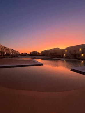 A serene waterfront view with buildings and a calm pool area during sunset.