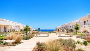 A resort with a pathway leading to a beach, featuring modern buildings and a clear view of the sea.