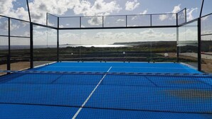 A tennis court with a net, surrounded by a black fence, and a clear view of the landscape.