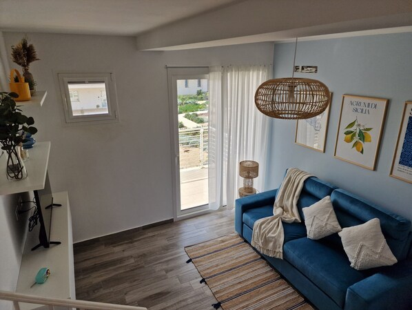 A living room with a blue sofa, a small rug, a hanging light fixture, and a window with curtains.