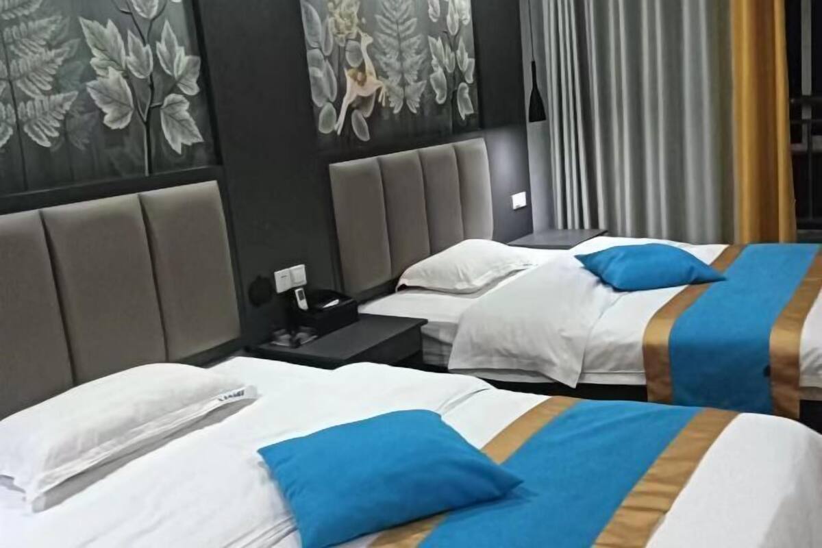 Habitación de hotel con dos camas, cada una con ropa de cama blanca y detalles azules, cabeceros grises y decoración floral en las paredes.