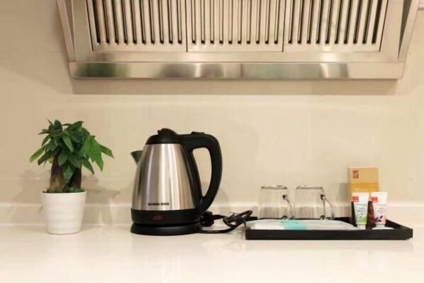 Una cocina con un hervidor de acero inoxidable, una planta en maceta y una bandeja con recipientes de vidrio y una caja.