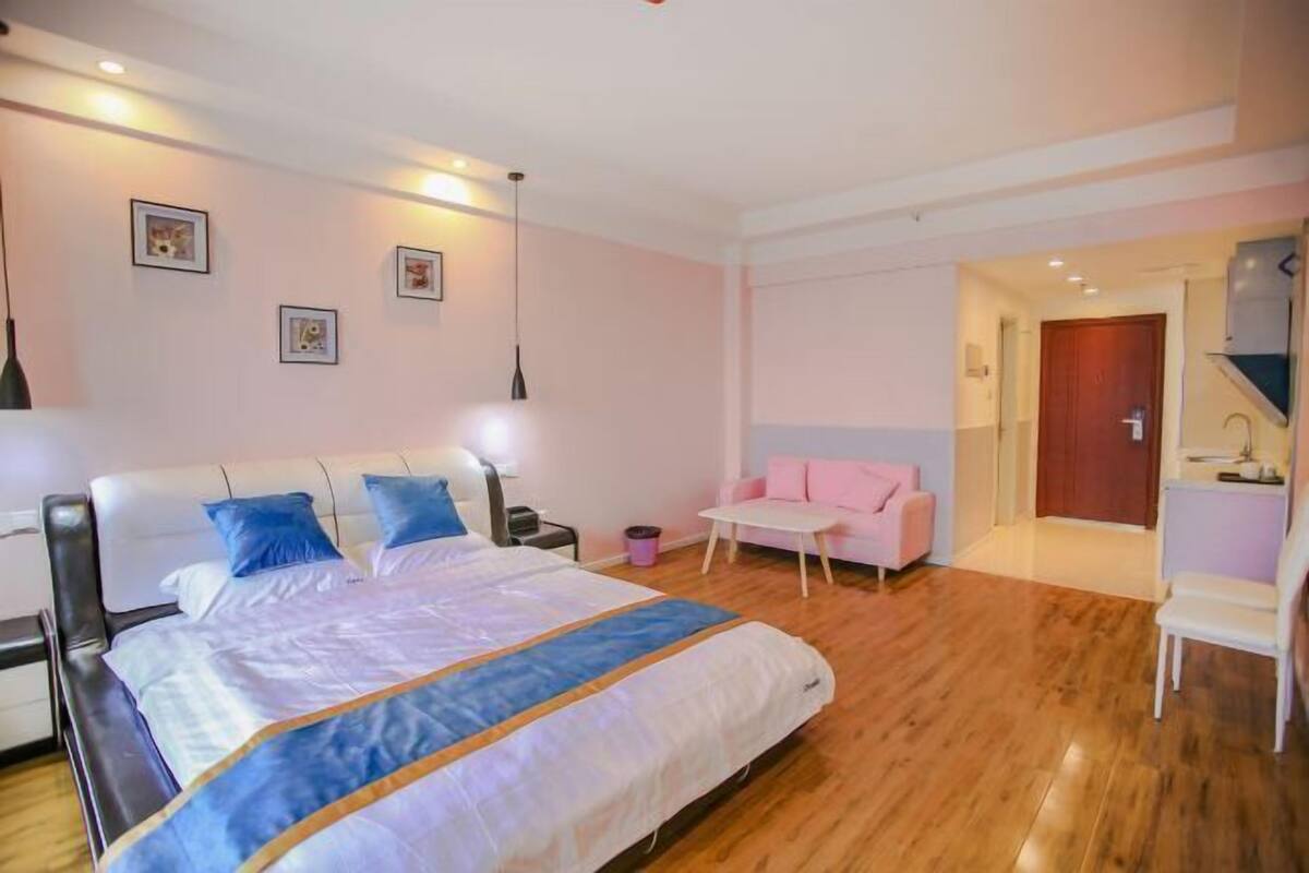 Un dormitorio con una cama grande, una mesita de noche, una silla, una pequeña mesa y una puerta que da a otra habitación.