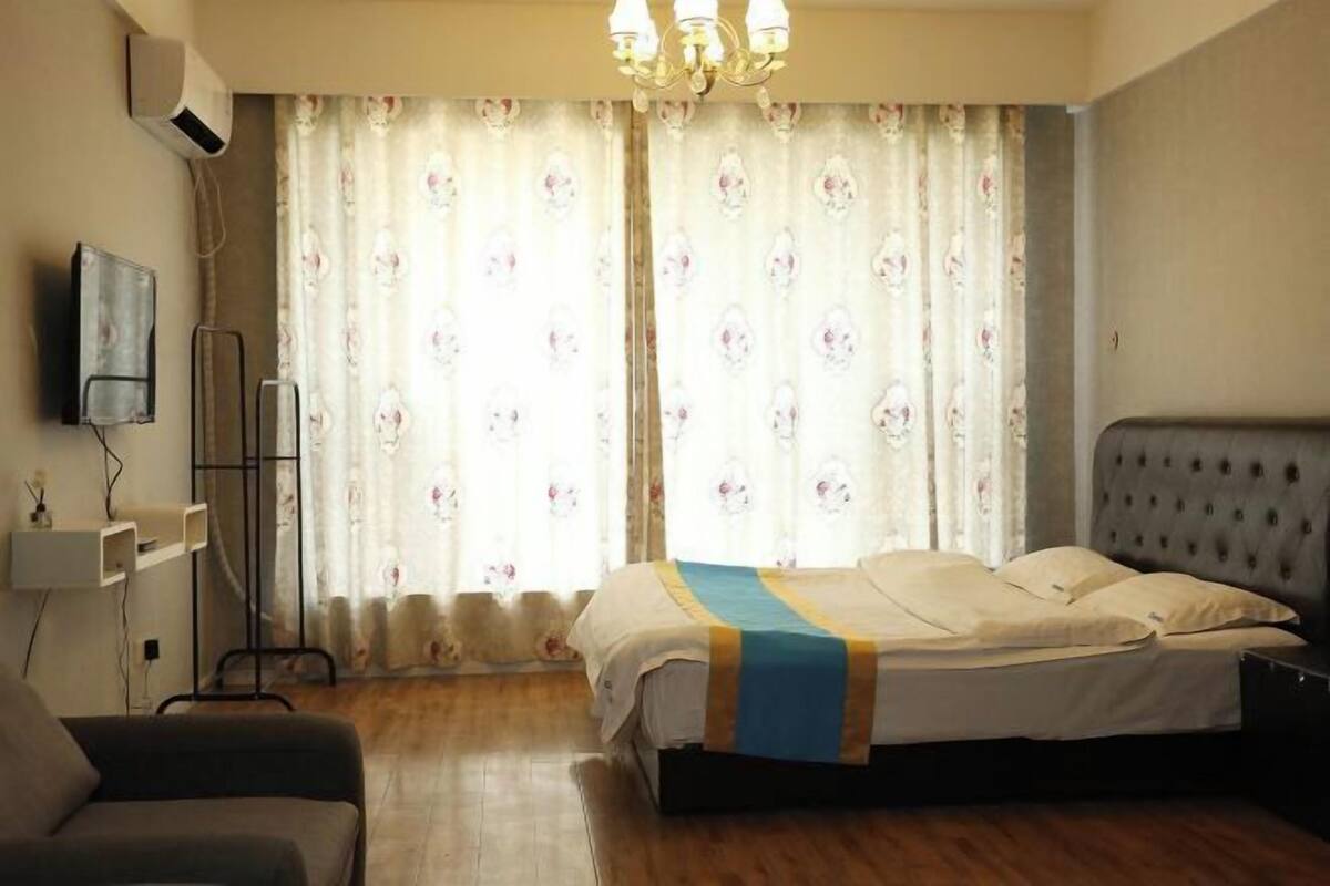 Un dormitorio con cama, mesita de noche, silla, televisor y ventana con cortinas.
