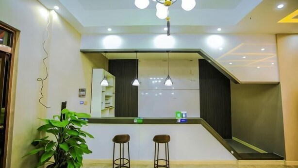 A reception area with a counter, two stools, a potted plant, and pendant lighting. - Yihaojing Boutique Hotel (Bengbu)