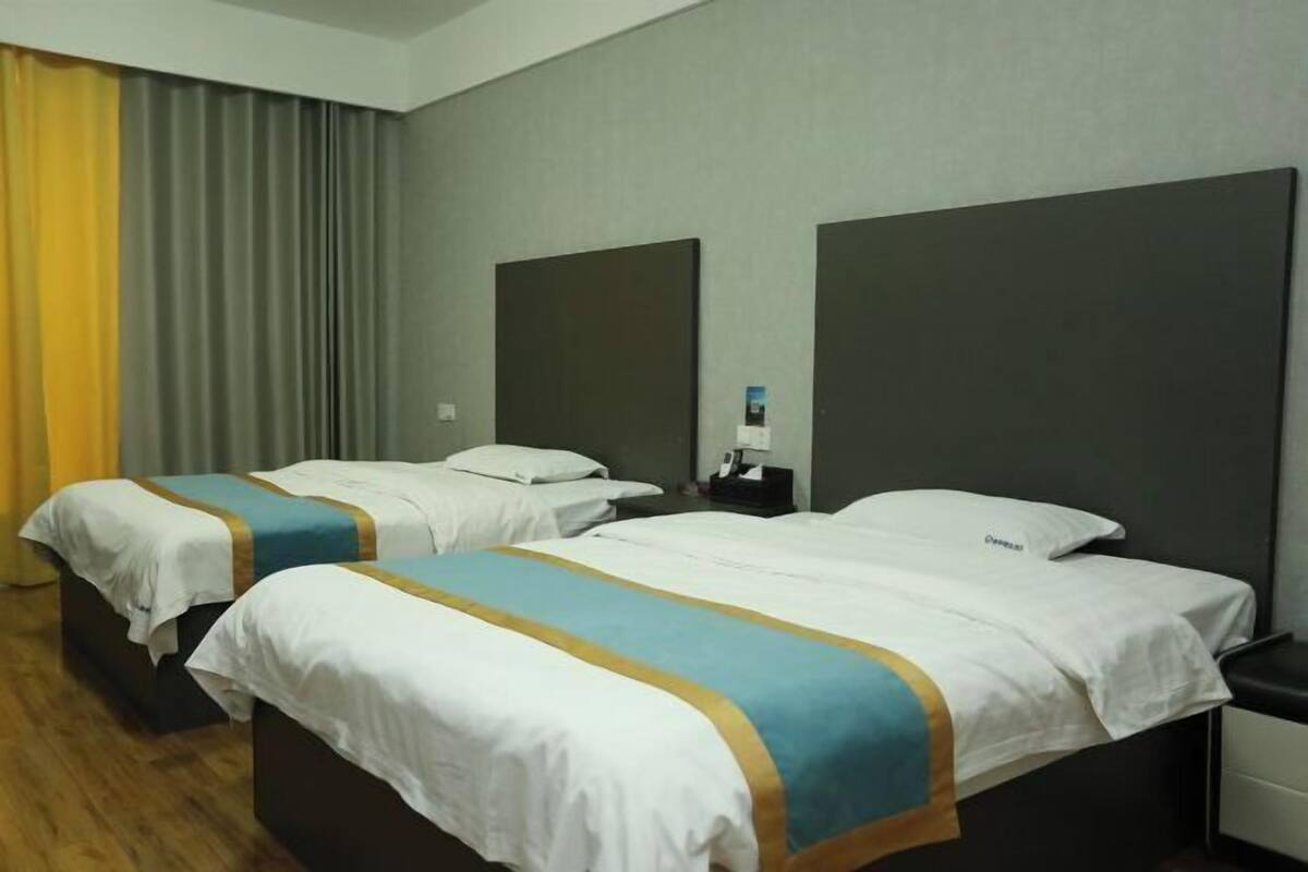 Habitación de hotel con dos camas, cada una con colcha a rayas blancas y azules, piso de madera y un ventanal con cortinas.