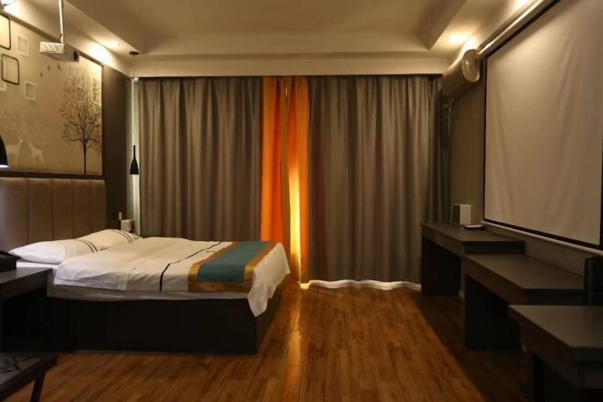 Habitación de hotel con cama, escritorio, silla, televisor y cortina.