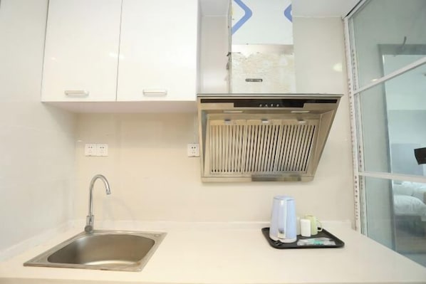 A modern kitchen with a stainless steel sink, white cabinets, and a built-in range hood. - Yihaojing Boutique Hotel (Bengbu)