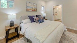 Une chambre avec un grand lit, deux tables de chevet avec des lampes, un tapis, un tableau au mur et une armoire avec un miroir.