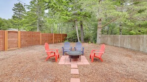 Une terrasse extérieure avec une table ronde et quatre chaises, entourée d’une clôture en bois et d’arbres.