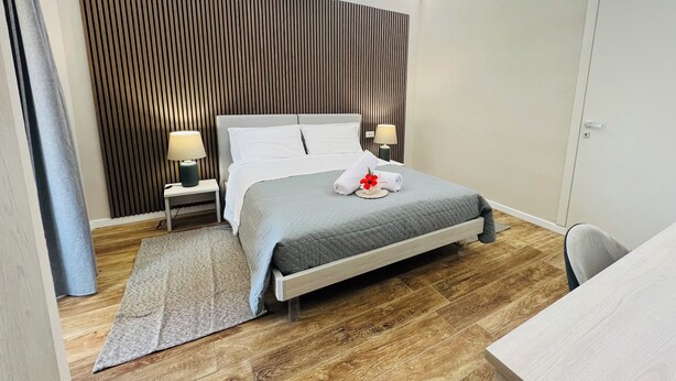 A modern hotel room with a bed, bedside lamps, a desk, and a wooden floor. - Maison Madeleine (La Maddalena)