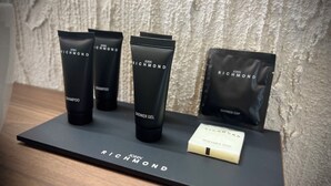A display of John Richmond products including shampoo, shower gel, and a shower cap on a black tray. - Maison Madeleine (La Maddalena)