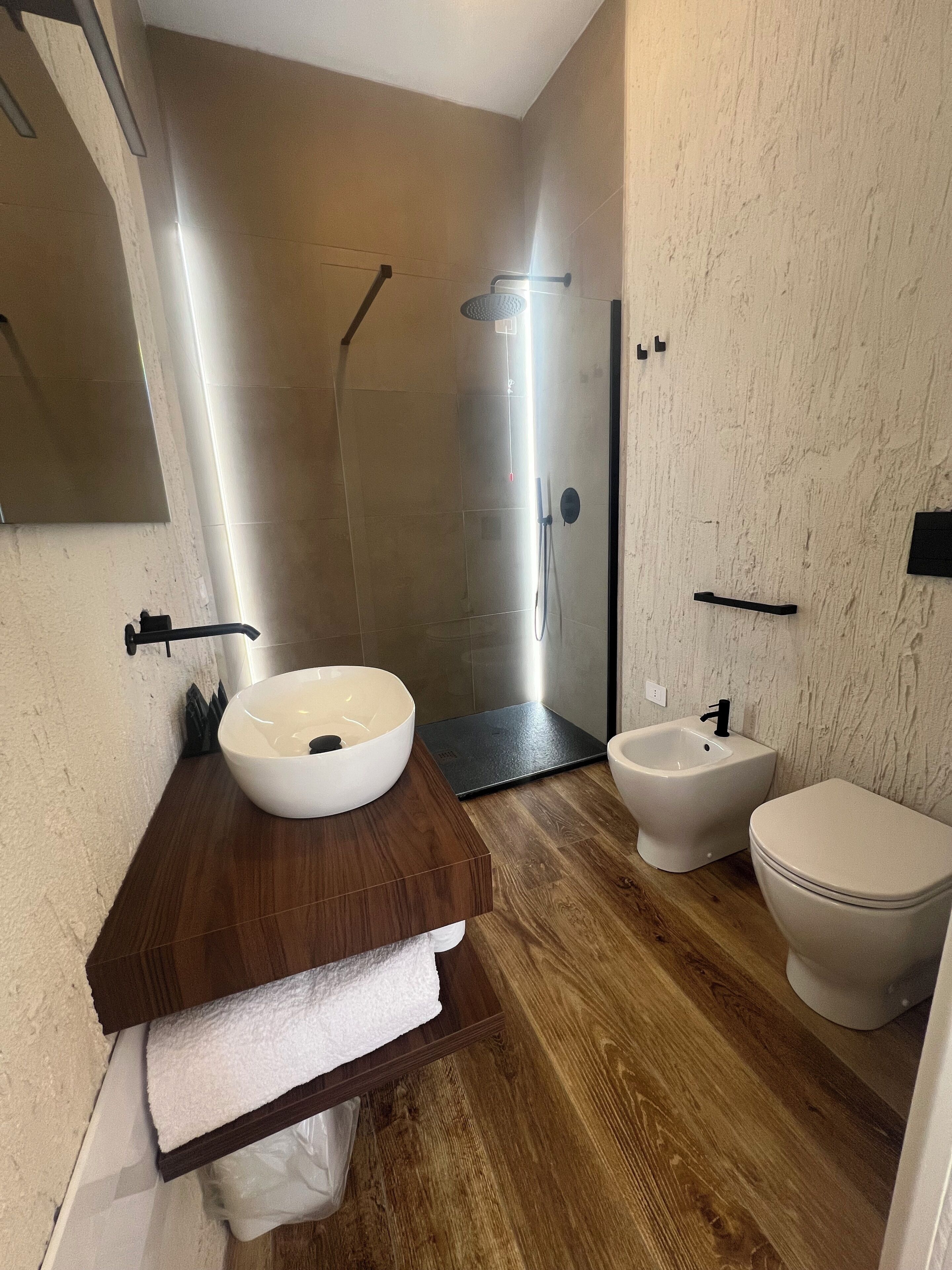 A modern bathroom with a wooden vanity, a white sink, a bidet, and a shower area.