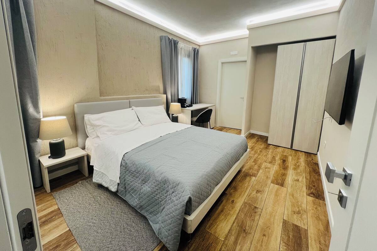 A modern hotel room with a large bed, bedside tables, a desk, and a wardrobe.