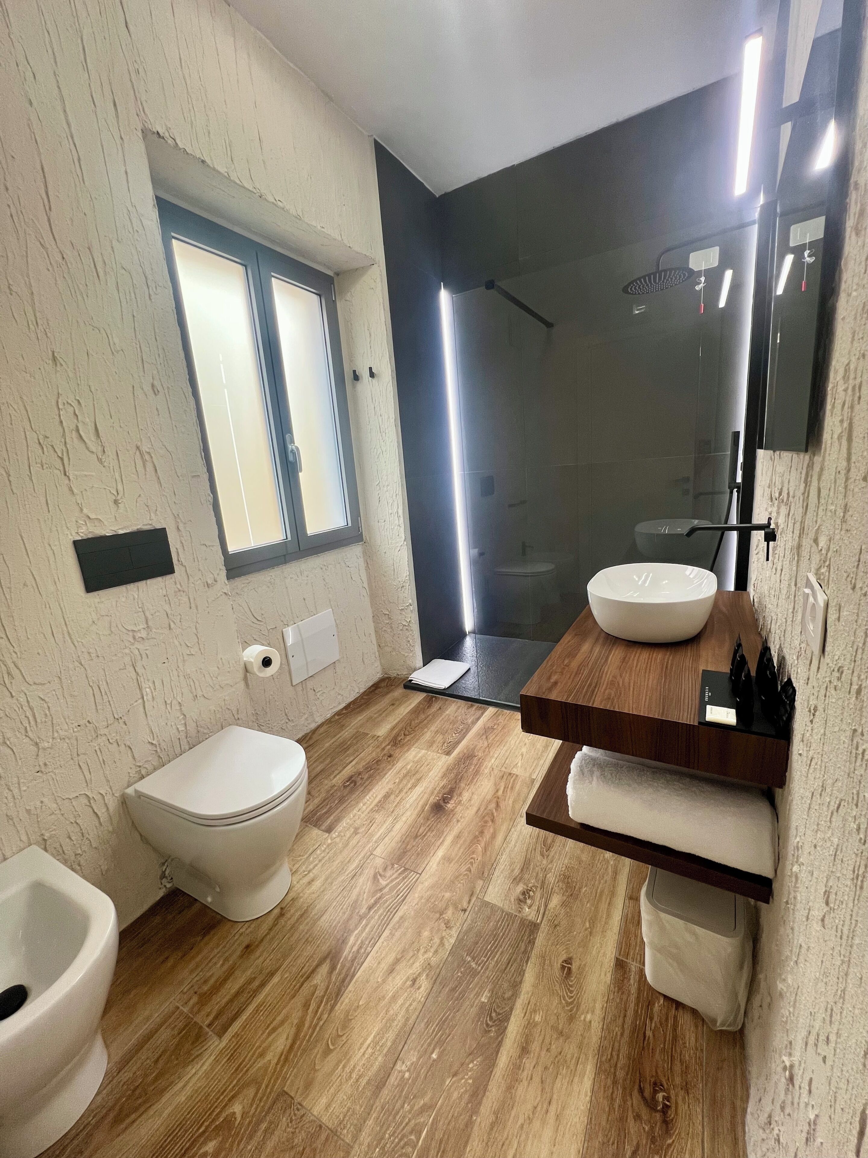A modern bathroom with a toilet, bidet, and a large mirror above a wooden vanity.