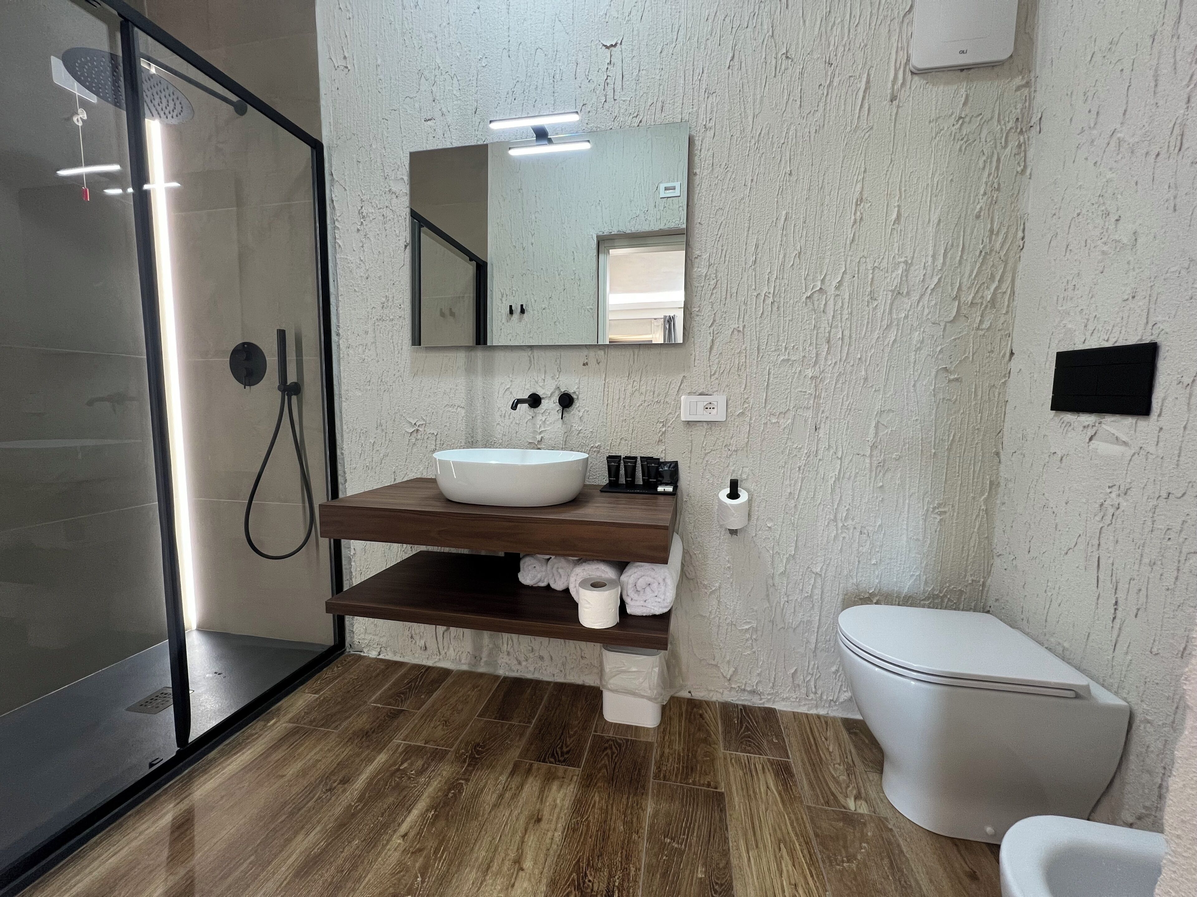 Een moderne badkamer met een douchecabine van glas, een houten wastafelmeubel met een witte wasbak en een toilet.