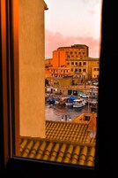 Vista dalla finestra su un porto con barche, edifici e un cielo rosa.