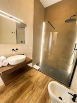 Un bagno moderno con doccia vetrata, un lavandino bianco e uno specchio grande.