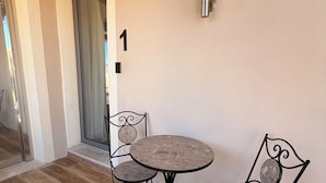 En patio med et rundt bord og to stole, en dør med et nummer og en vægmonteret lampe.