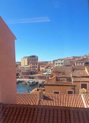 Eine Küstenstadt mit terrakottafarbenen Dächern, einem Yachthafen mit Booten und einem wolkenlosen, blauen Himmel.