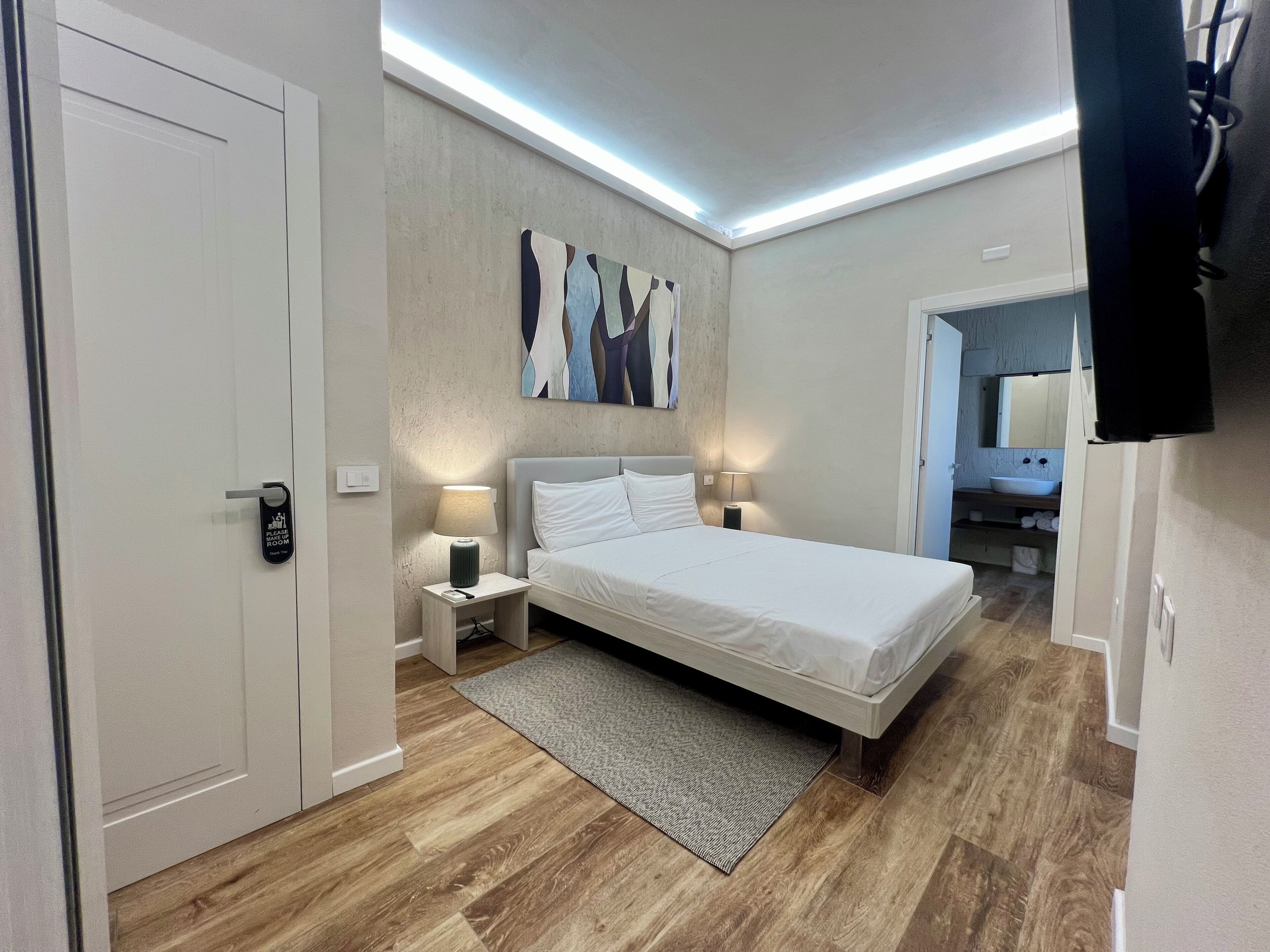 Habitación de hotel con cama, lámparas de noche, alfombra, un cuadro en la pared y una puerta con un letrero.