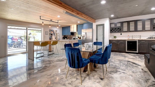Een moderne keuken met een marmeren vloer, een eethoek met blauwe fluweelstoelen, en een bar met gele stoelen.