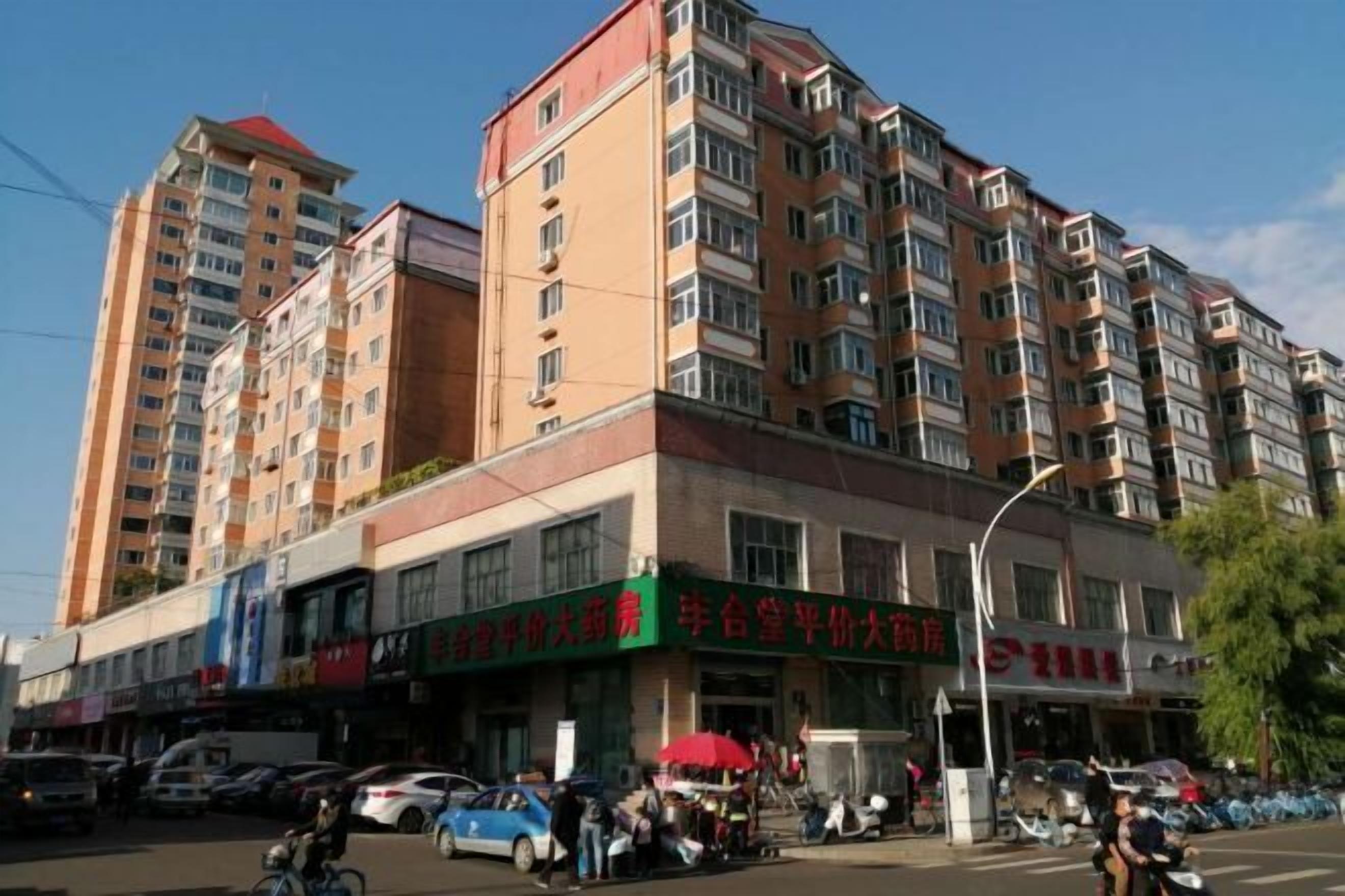 Un immeuble à plusieurs étages dont le rez-de-chaussée est occupé par des commerces, notamment une pharmacie et un restaurant.