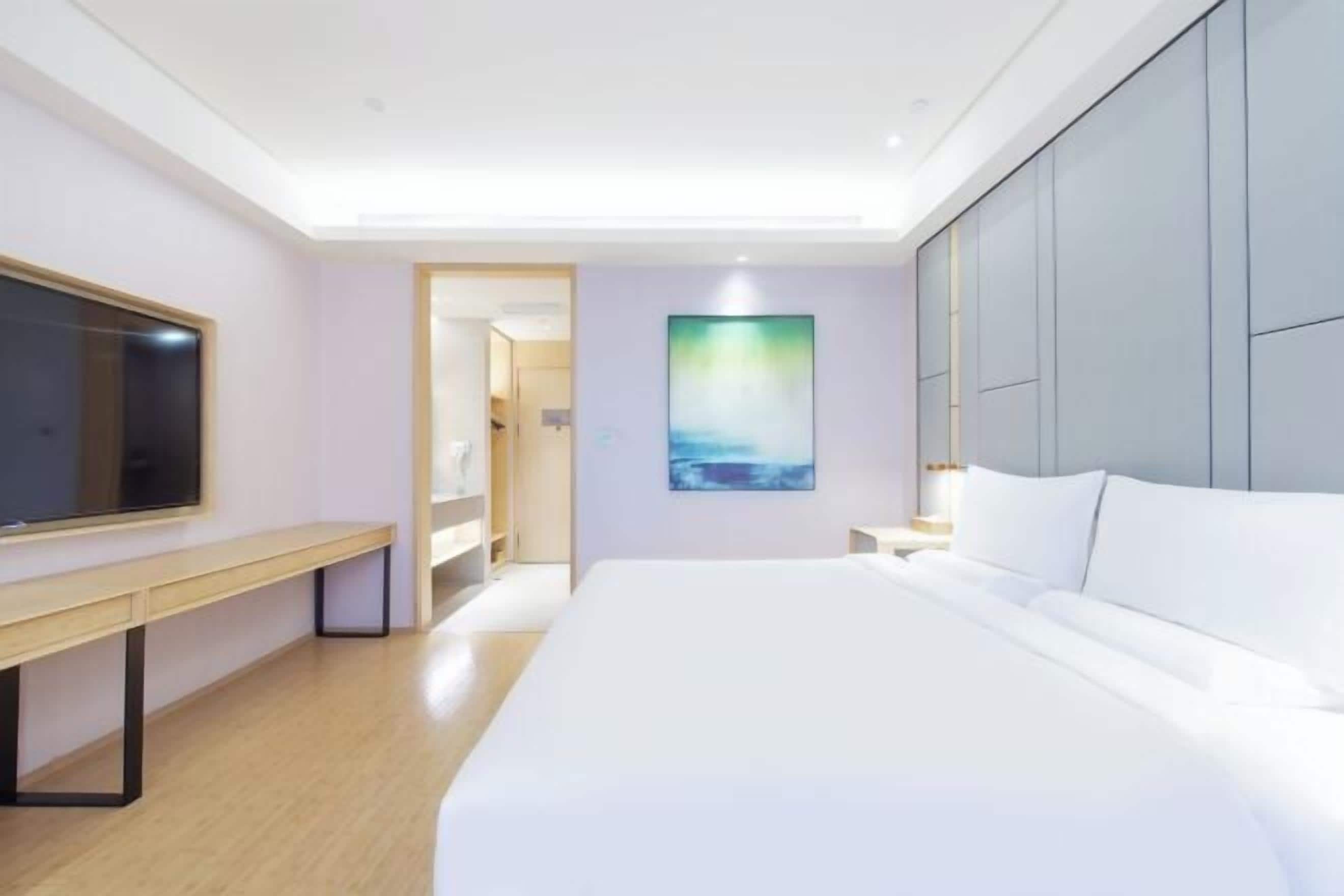 Habitació d'hotel moderna amb un llit gran, una televisió de pantalla plana, una banca i un quadre a la paret.