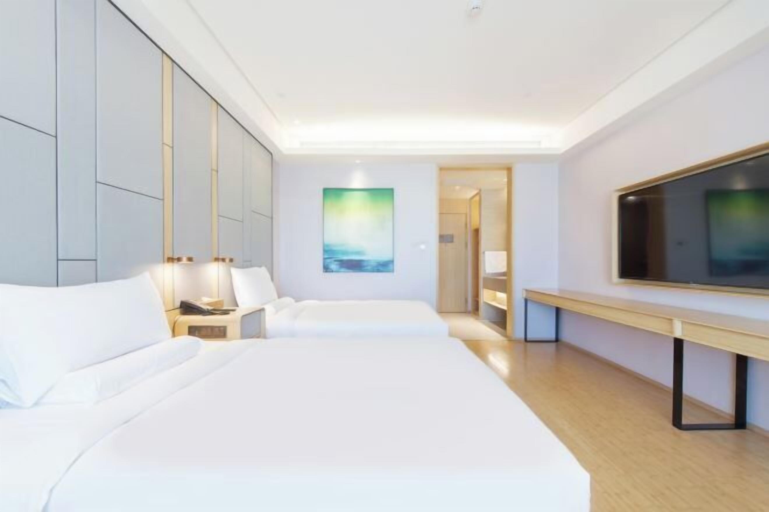 A hotel room with a large bed, bedside tables, a TV, and a painting on the wall.