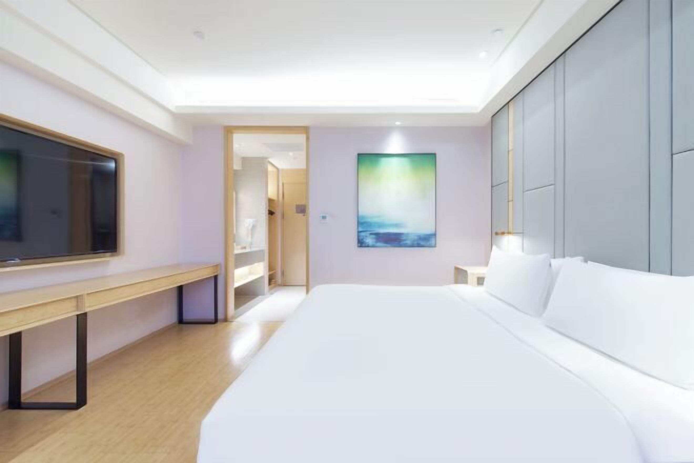 Et moderne hotelværelse med en stor seng, et fladskærms-tv, et skrivebord og et maleri på væggen.