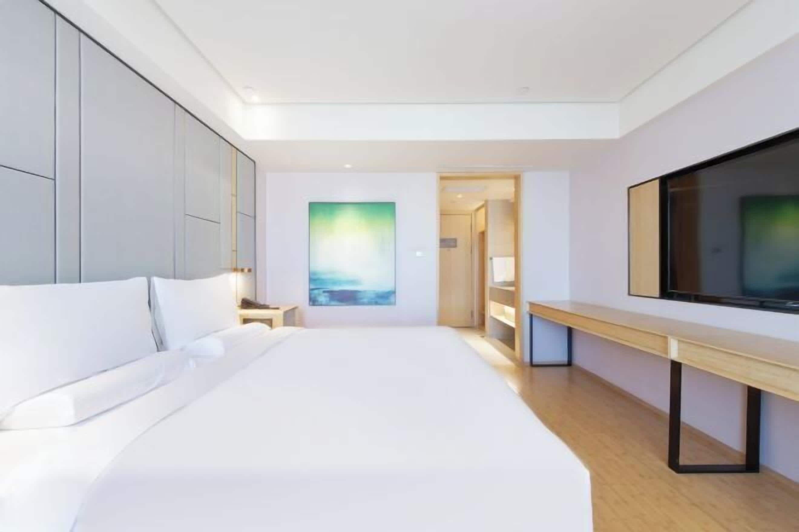 Quarto de hotel moderno com uma cama grande, televisão de tela plana, um quadro na parede e um banco de madeira.
