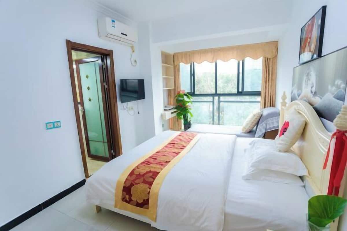 Una habitación de hotel con una cama, televisión, ventana con cortinas y una planta.