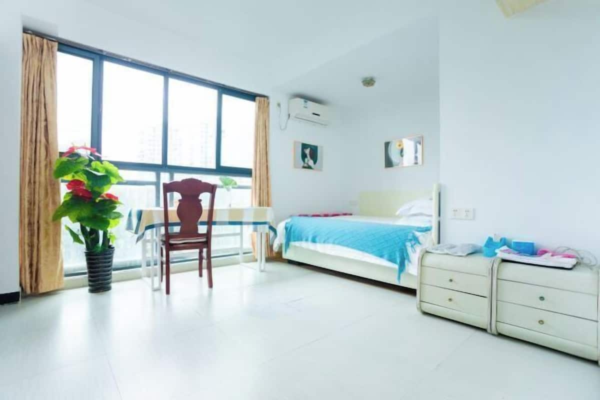 Un dormitorio con cama, mesita de noche, silla y un ventanal grande.