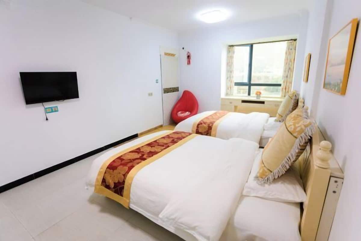 Habitación de hotel con dos camas, un televisor de pantalla plana, una silla roja, un ventanal con vistas y una puerta.