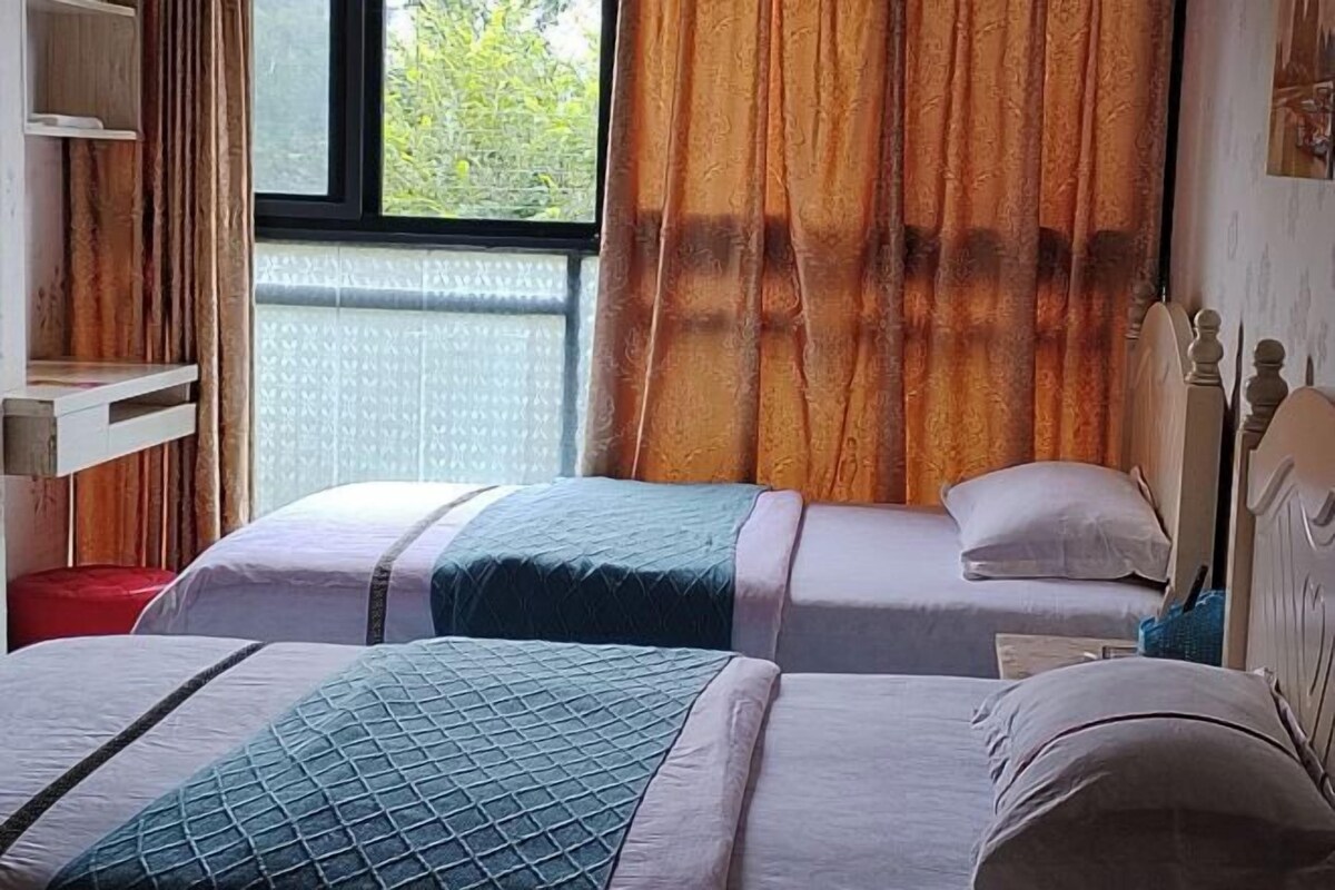 A hotel room with two beds, a window with curtains, a wooden headboard, and a small shelf.