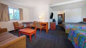 A hotel room with a bed, a desk, two chairs, a small table, and a TV. - Unicorn Inn by OYO Portland (Portland)