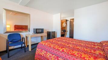 Una habitación de hotel con cama, un escritorio con silla, televisor y armario.