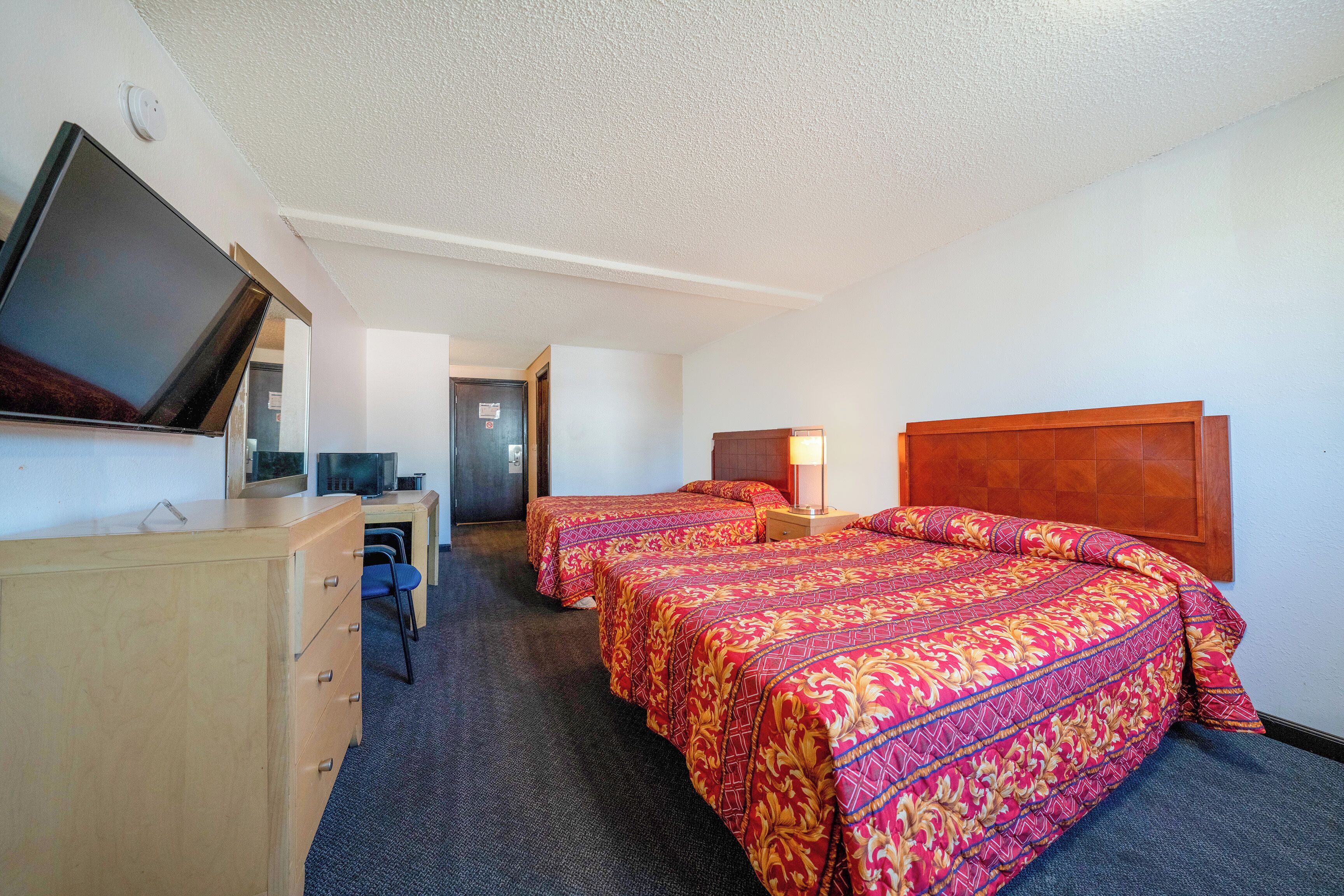 Habitación de hotel con dos camas, un escritorio, un televisor y una puerta que da a otra habitación.