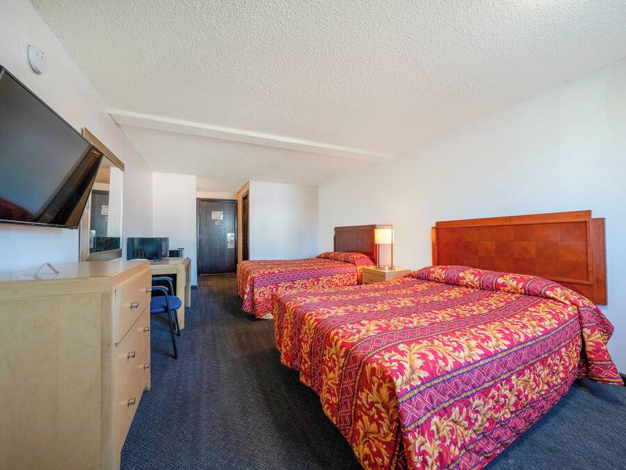 Une chambre d’hôtel avec deux lits, un bureau, une télévision et une porte donnant sur une autre chambre.